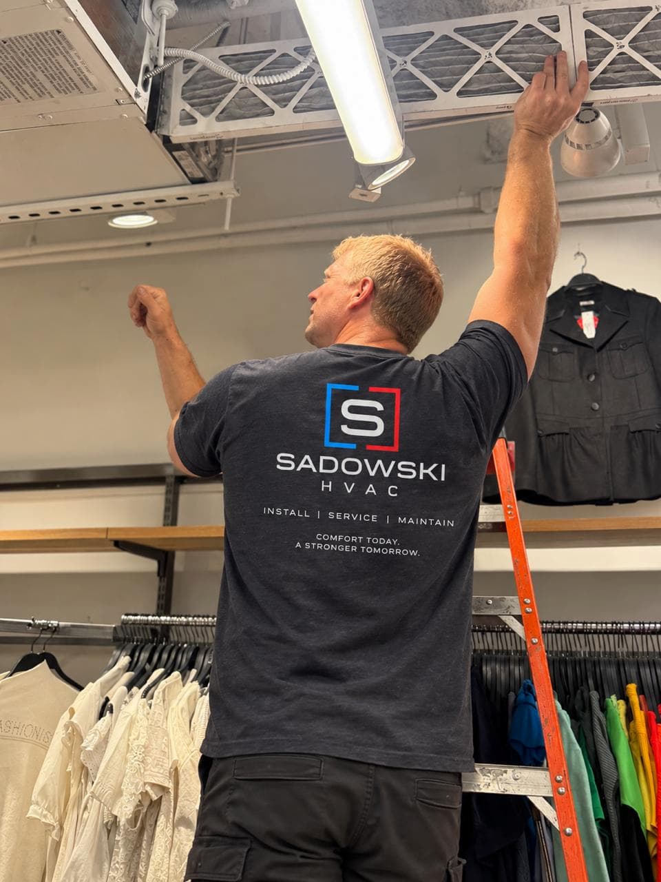 Sadowski HVAC technician accessing ceiling-mounted equipment during commercial filter service