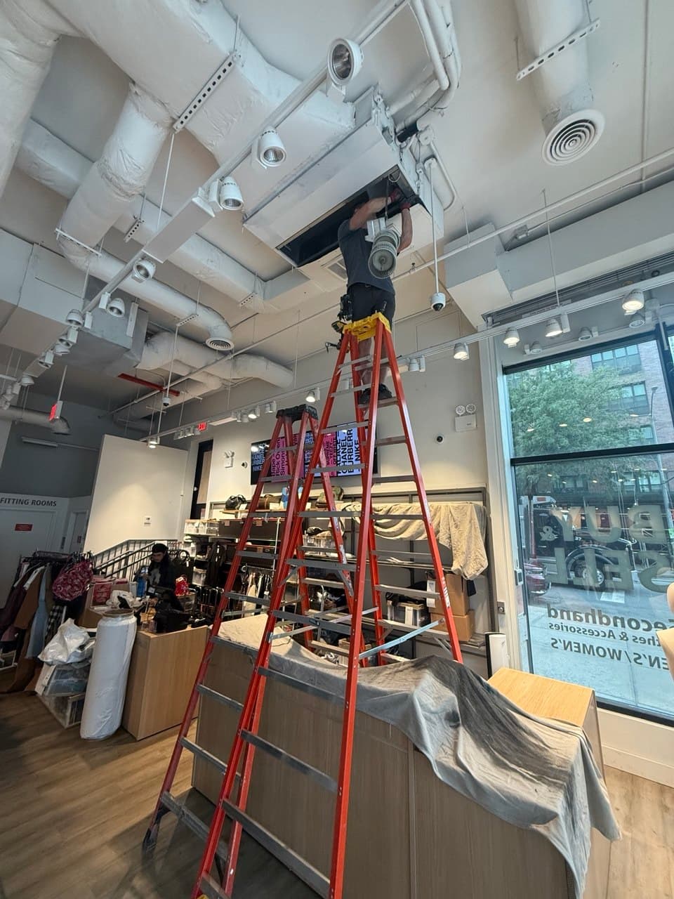 Commercial HVAC technician accessing a ceiling-mounted indoor unit in a retail store