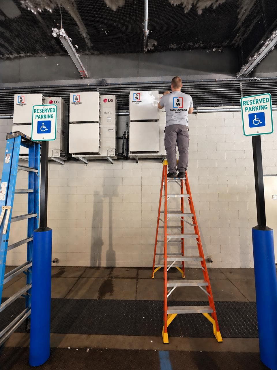 Sadowski HVAC technician servicing wall-mounted LG VRF equipment from a ladder